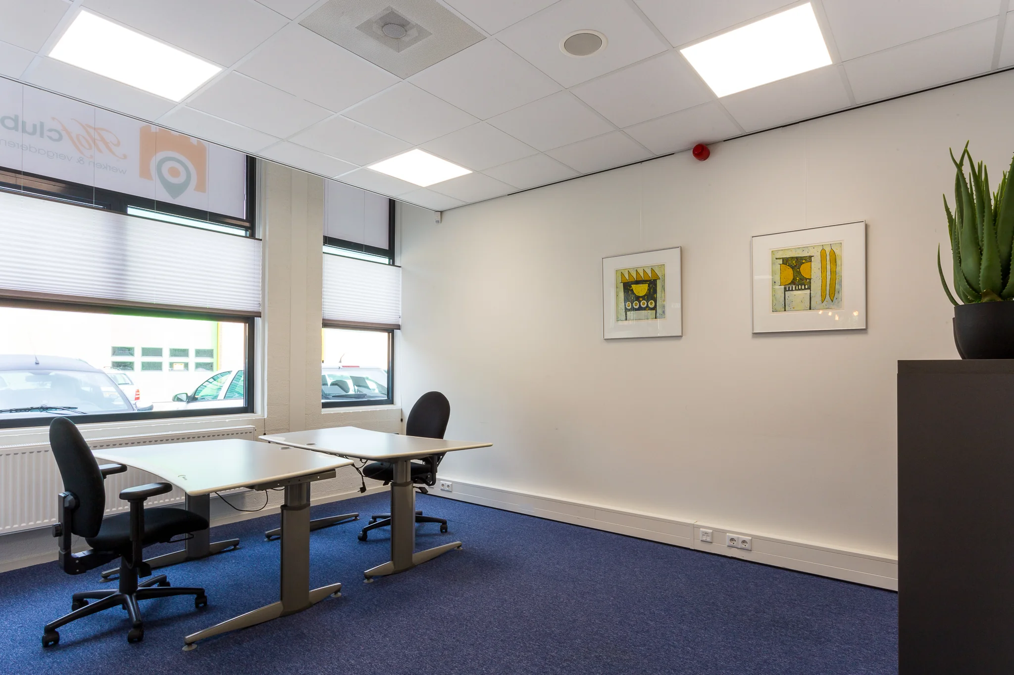 Twee werkplekken in een licht kantoor aan de Niels Bohrweg met moderne inrichting en kunst aan de muur.